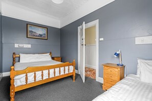 Ein Schlafzimmer mit einem hölzernen Bett, einem Nachttisch, einer Kommode, einer Tür und einem an der Wand befestigten Lichtschalter.
