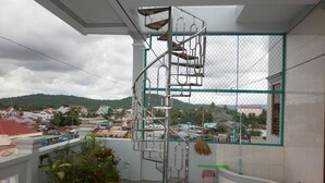A balcony with a metal spiral staircase, potted plants, and a view of a town with buildings and hills. - Hai Hien Guesthouse Phu Quoc (Phu Quoc)