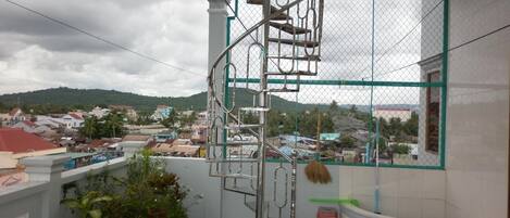 A balcony with a metal spiral staircase, potted plants, and a view of a town with buildings and hills.