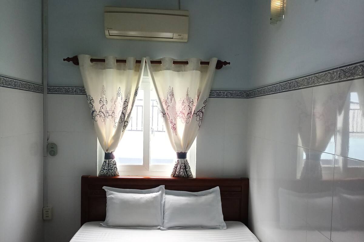 Ein Hotelzimmer mit einem Bett, einem Vorhangfenster, einer Klimaanlage und einem Bild an der Wand.