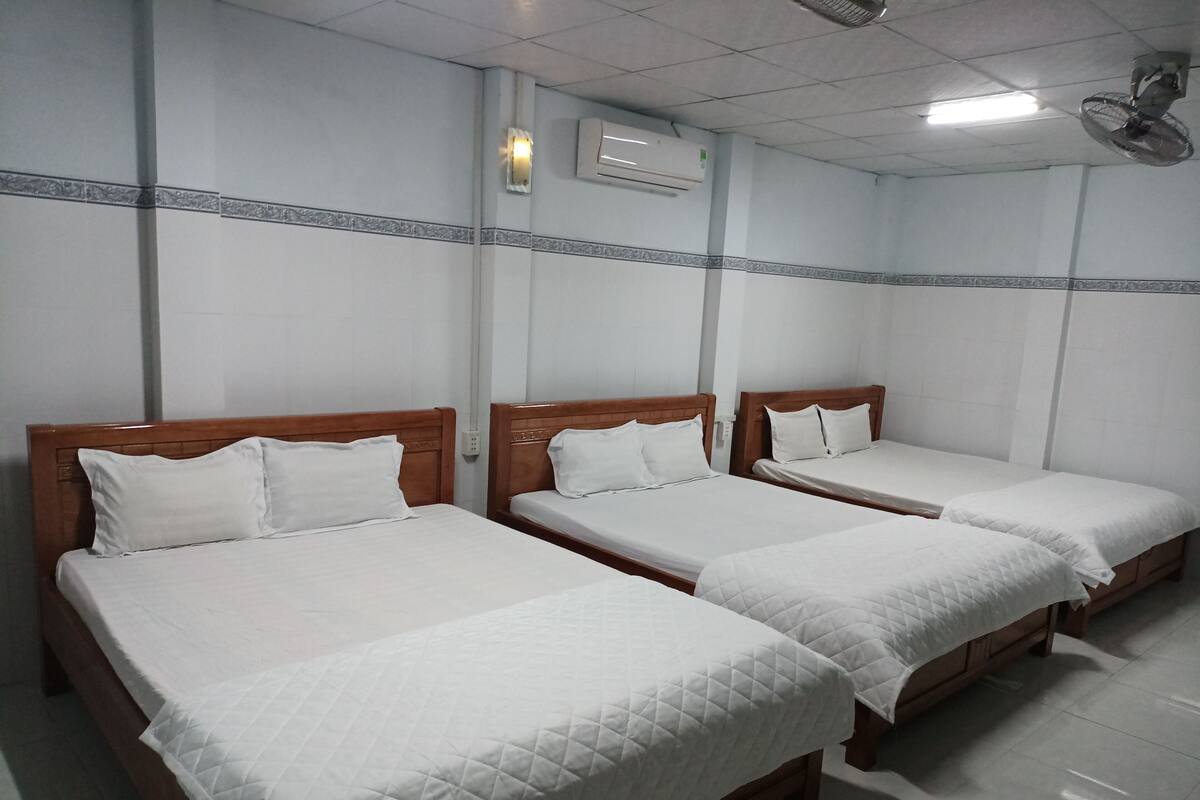 Ein Hotelzimmer mit vier Einzelbetten, jedes mit einem hölzernen Kopfteil und weißer Bettwäsche.