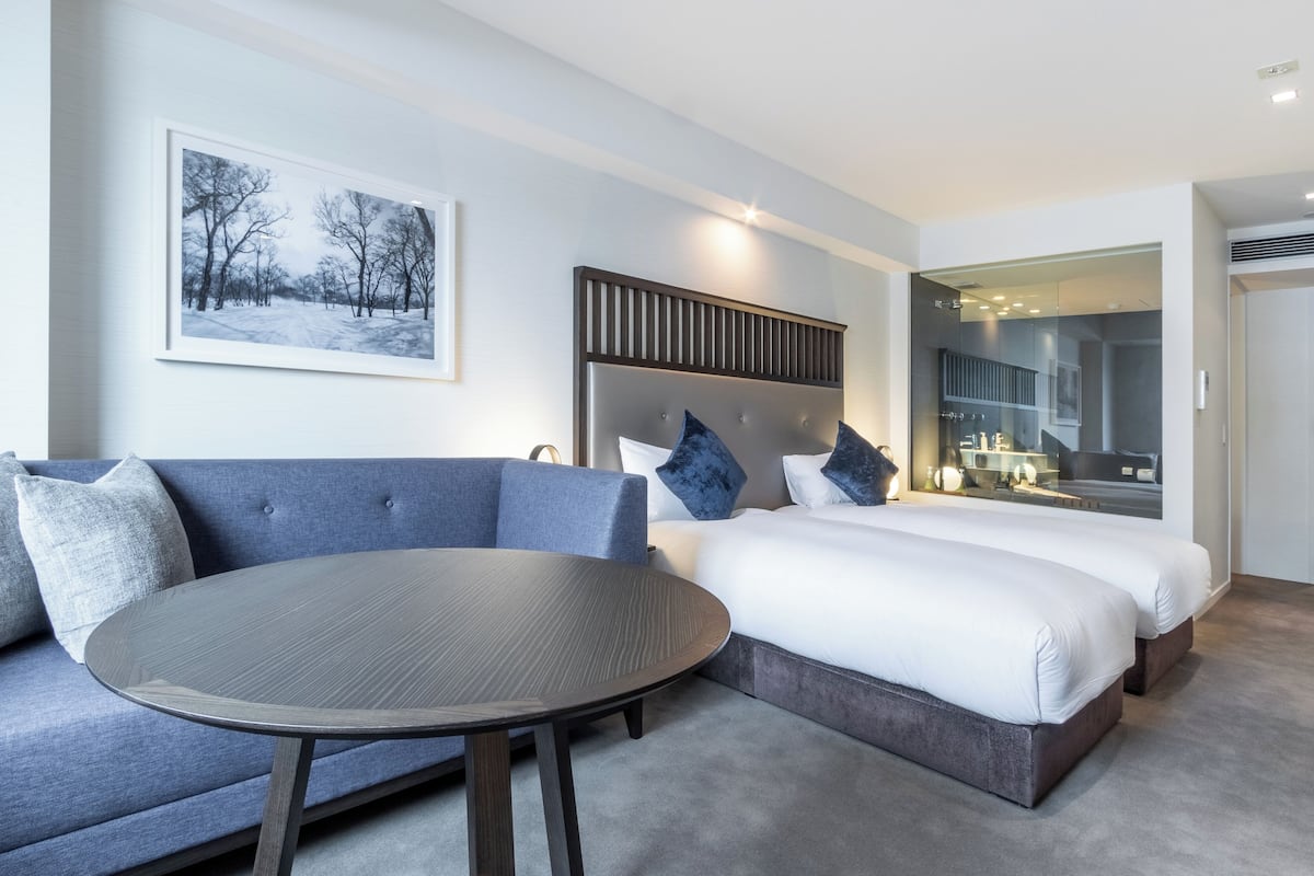 Habitación de hotel moderna con una cama grande, un sofá, una mesa redonda y un cuadro en la pared.