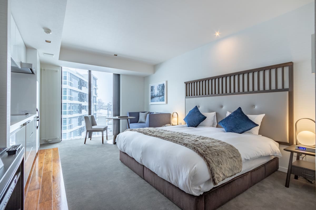 Habitación de hotel moderna con una cama grande, zona de estar y vistas a la ciudad.