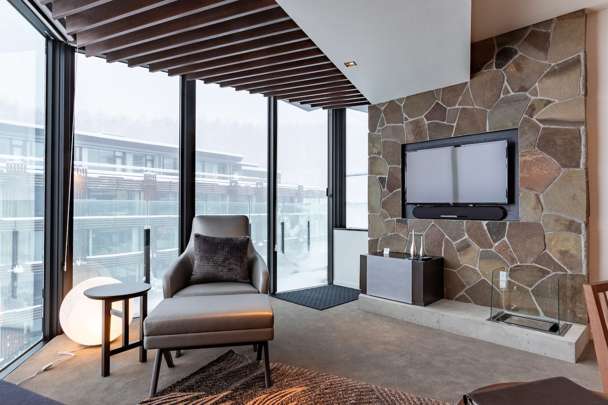 Un salón moderno con chimenea de piedra, un televisor de pantalla plana, un sofá y ventanas amplias que ofrecen vista a la ciudad.