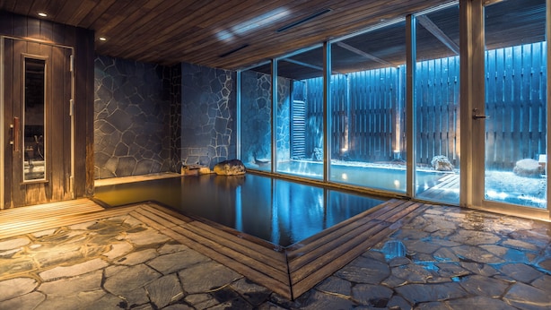 A spa area with a stone floor, wooden ceiling, and glass walls. - The Vale Niseko (Kutchan)