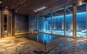 A spa area with a stone floor, wooden ceiling, and glass walls. - The Vale Niseko (Kutchan)