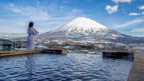 A person in a polka dot dress overlooking a snow-capped mountain from a pool area. - The Vale Niseko (Kutchan)