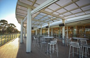 Un espace extérieur aménagé en terrasse, avec des tables et des chaises, protégé par un toit de verre et offrant une vue sur le paysage environnant.