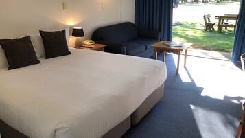 A hotel room with a large bed, a sofa, a small table, and a view of a park.