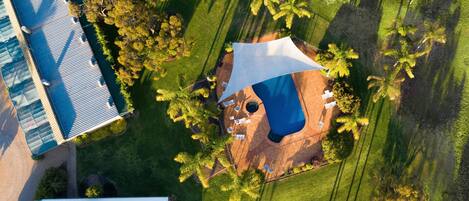 Vue aérienne d’une propriété dotée d’une piscine, d’un espace extérieur couvert et d’un jardin luxuriant.