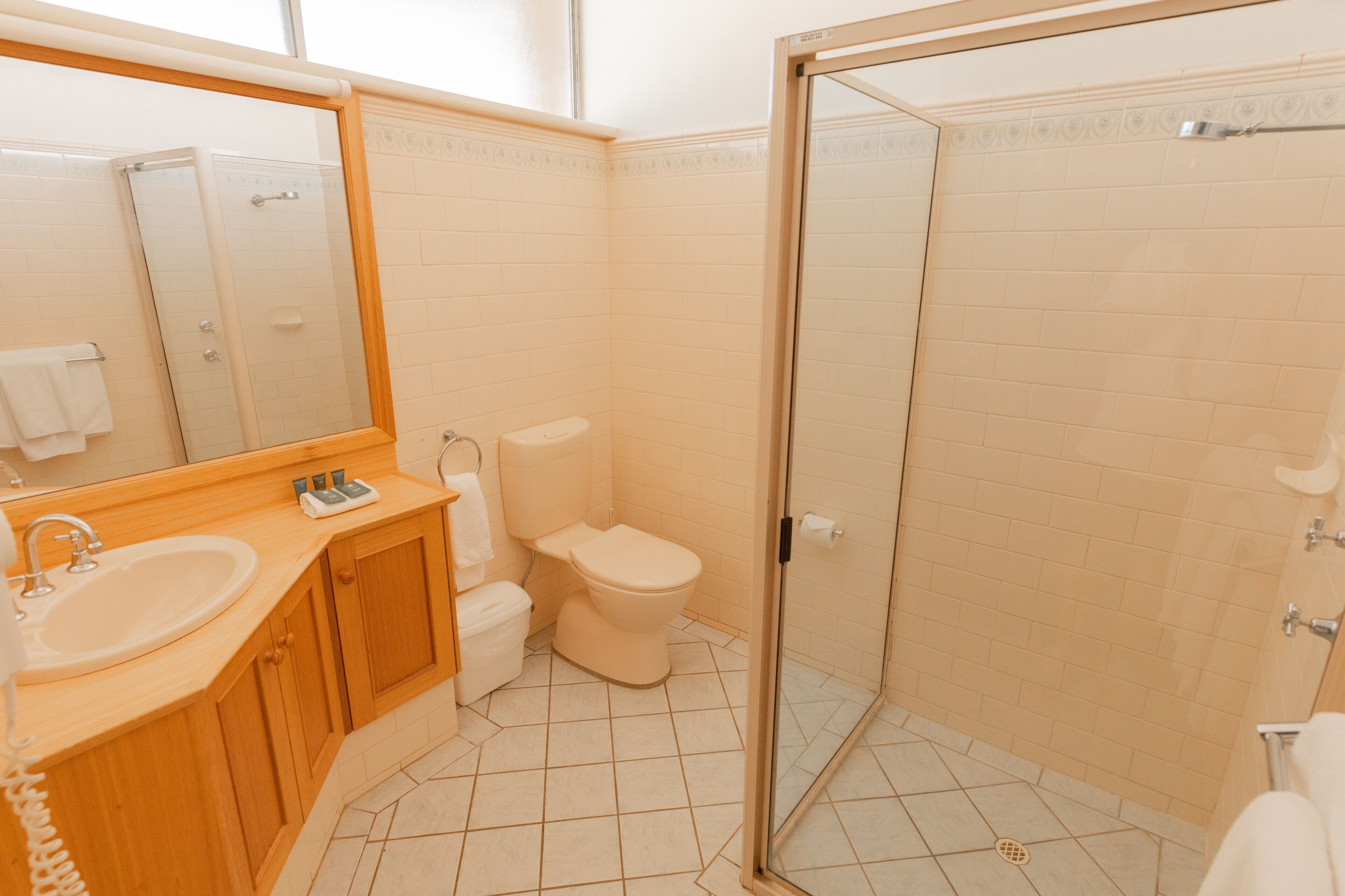 Un baño con tocador de madera, lavamanos, inodoro y ducha con cerramiento de vidrio.