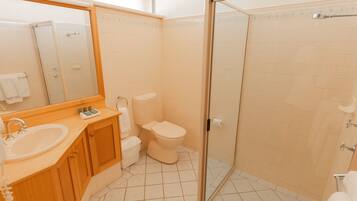 Un baño con tocador de madera, lavamanos, inodoro y ducha con cerramiento de vidrio.