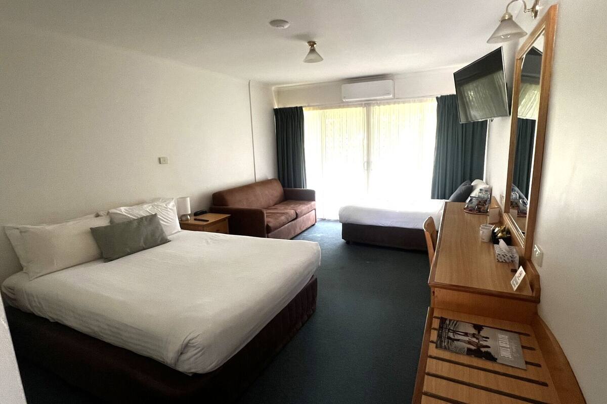 A hotel room with a large bed, a sofa, a desk, and a mirror.