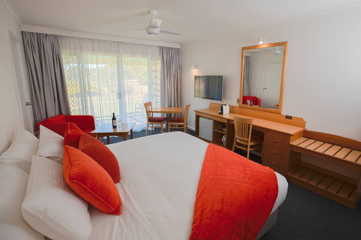 A hotel room with a large bed, a desk, a chair, a TV, and a mirror.