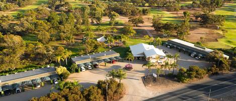Vista aérea de un campo de golf con un club de campo, área de estacionamiento y un edificio grande con techo plano.