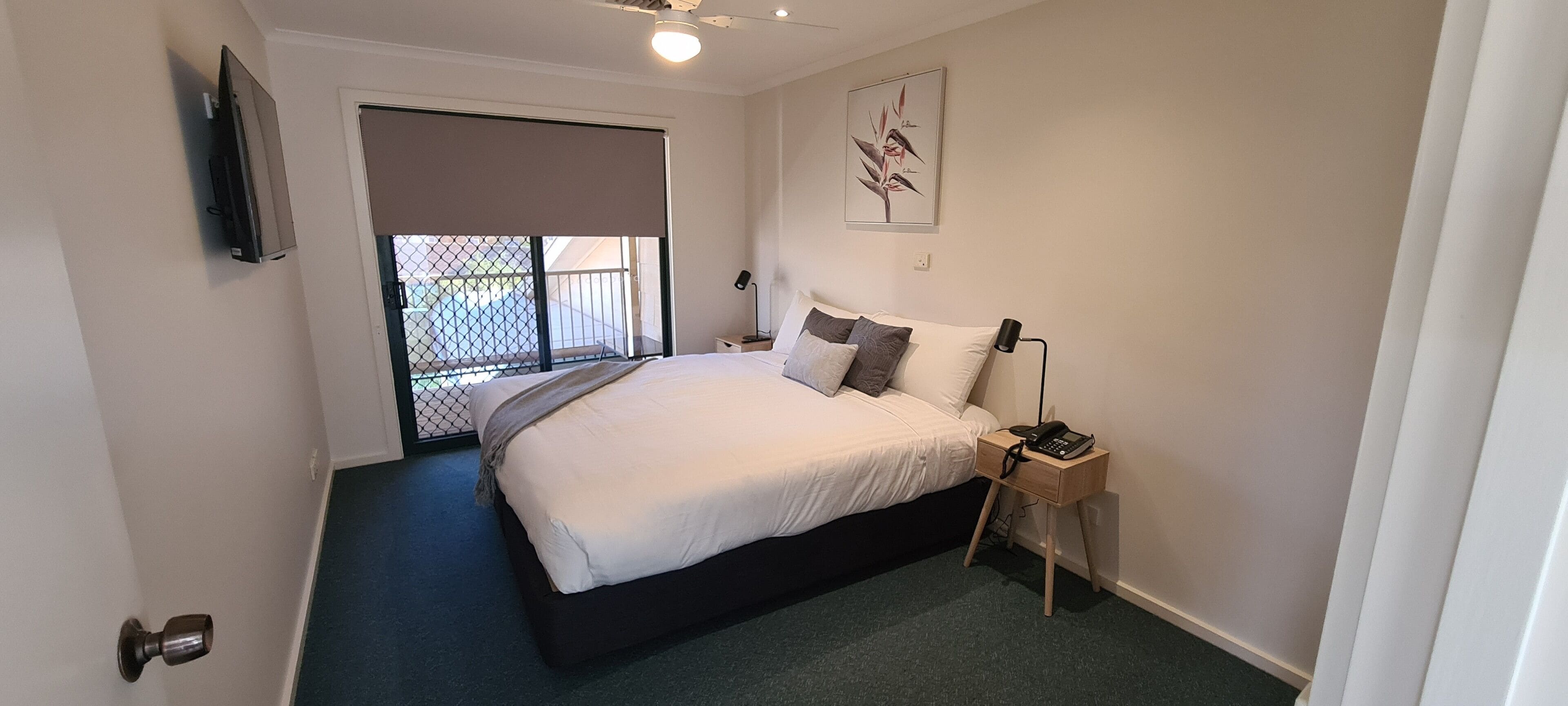 Un dormitorio con cama, mesita de noche, lámpara y vistas al exterior.