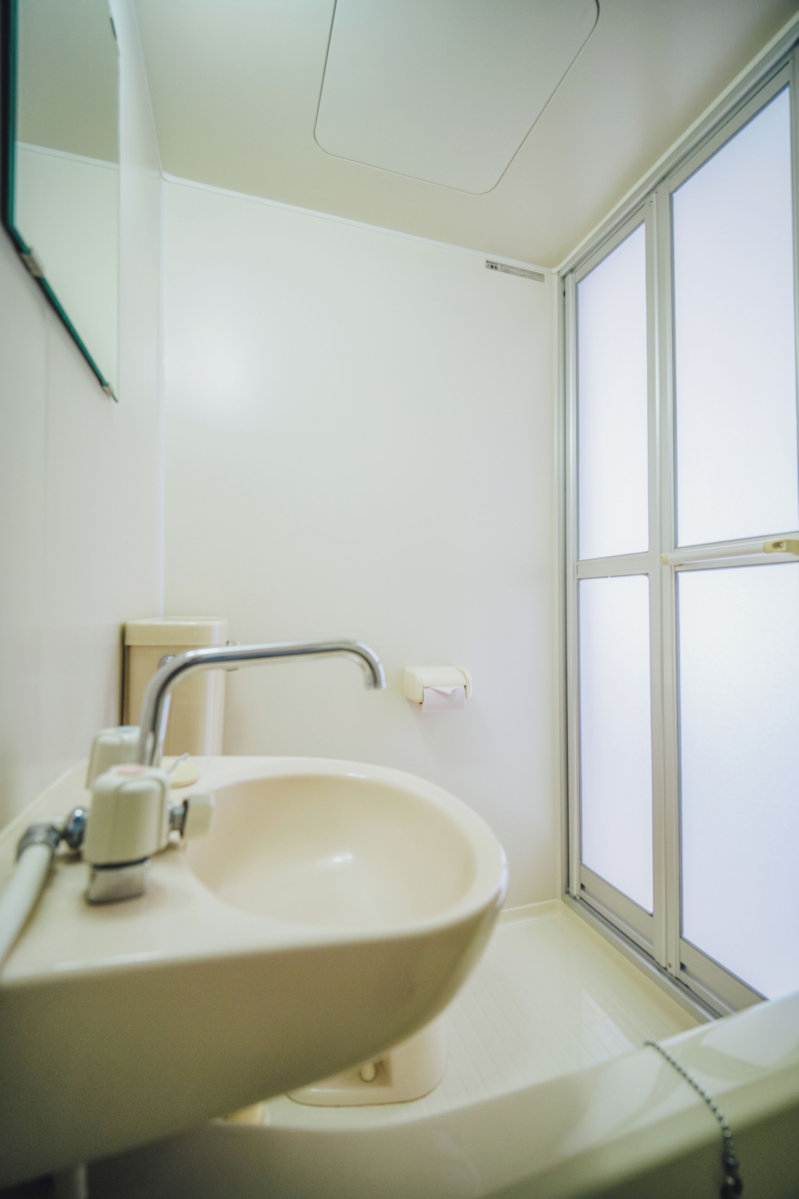 Un baño con lavamanos blanco, espejo y ventana.