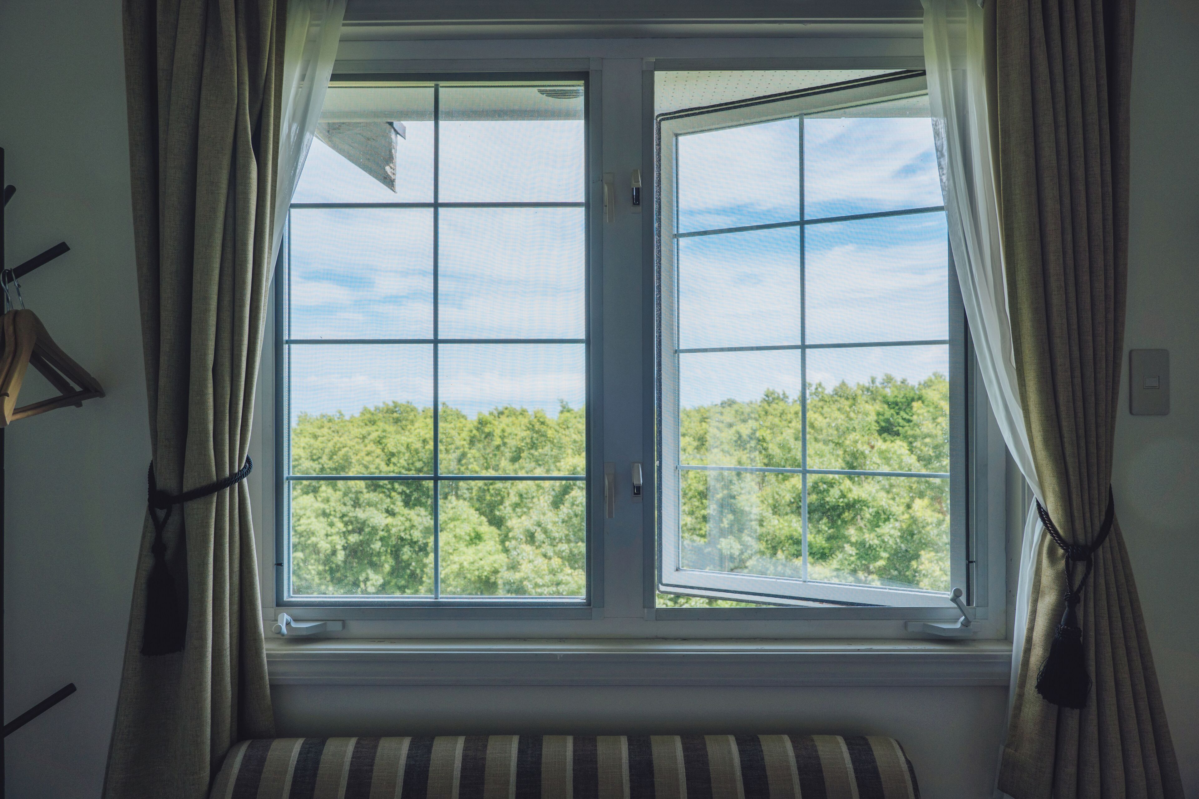 A room with a large window, curtains, a radiator, and a striped cushion.