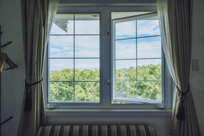 Una habitación con un ventanal grande, cortinas, un radiador y un cojín a rayas.