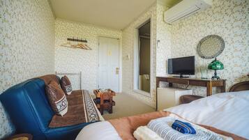 Una habitación de hotel con cama, sofá azul, escritorio con televisor y armario.