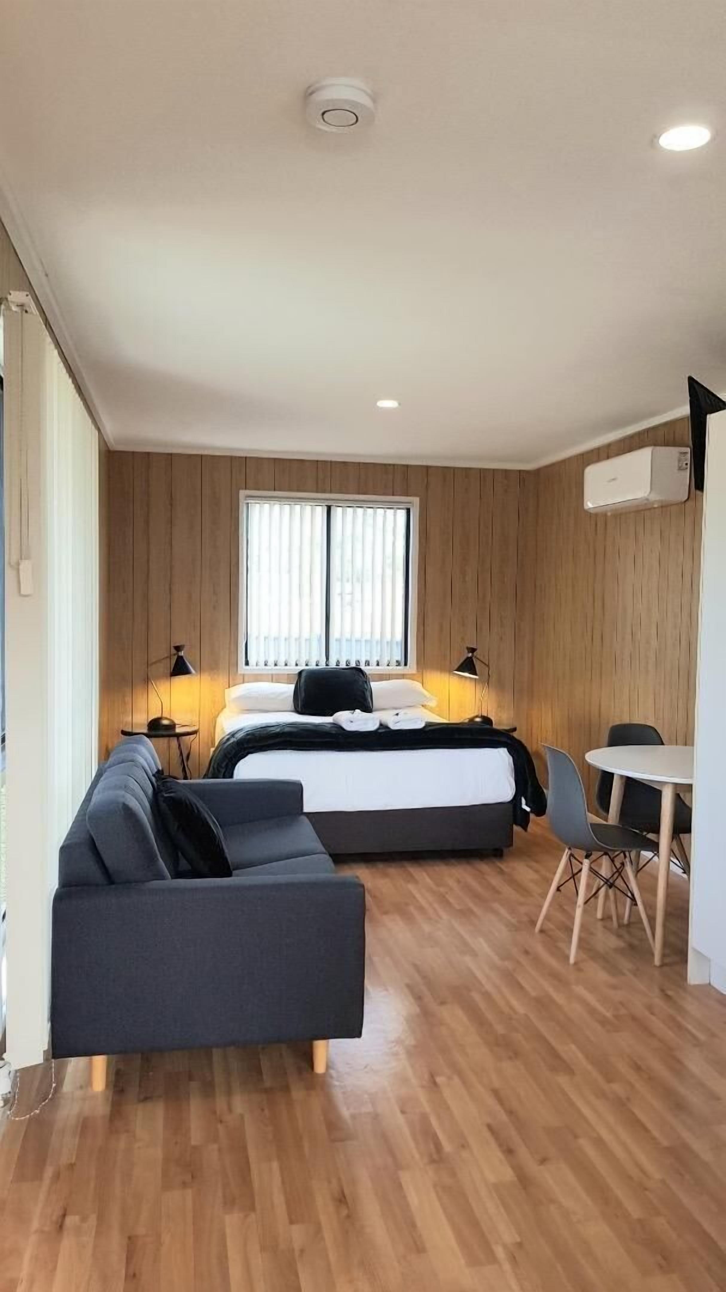 A modern room with a bed, a sofa, a dining table, and a window with blinds.