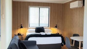 A modern room with a bed, a sofa, a dining table, and a window with blinds.