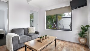 Un salon moderne avec un canapé gris, une table basse en bois et une grande fenêtre donnant sur une maison et des arbres.