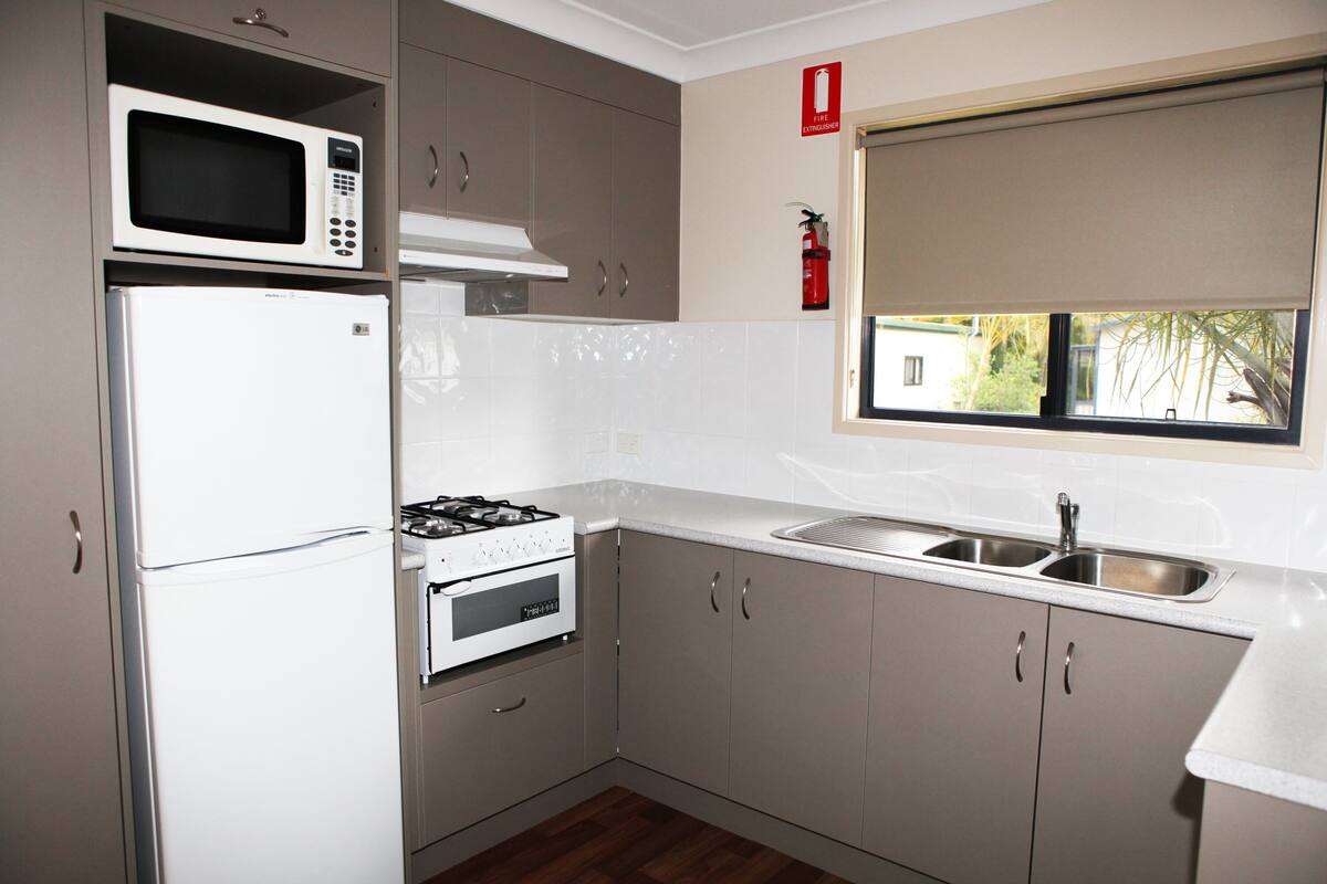 Cocina compacta con microondas, refrigerador, estufa, horno y ventana con vista a la vegetación.