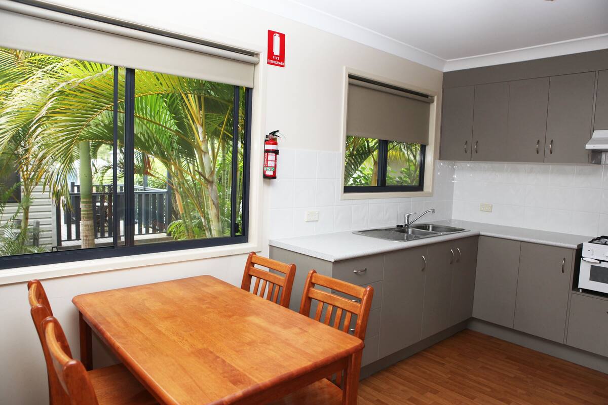 Una cocina moderna con una mesa de comedor de madera, armarios grises y una ventana con vistas a un jardín.