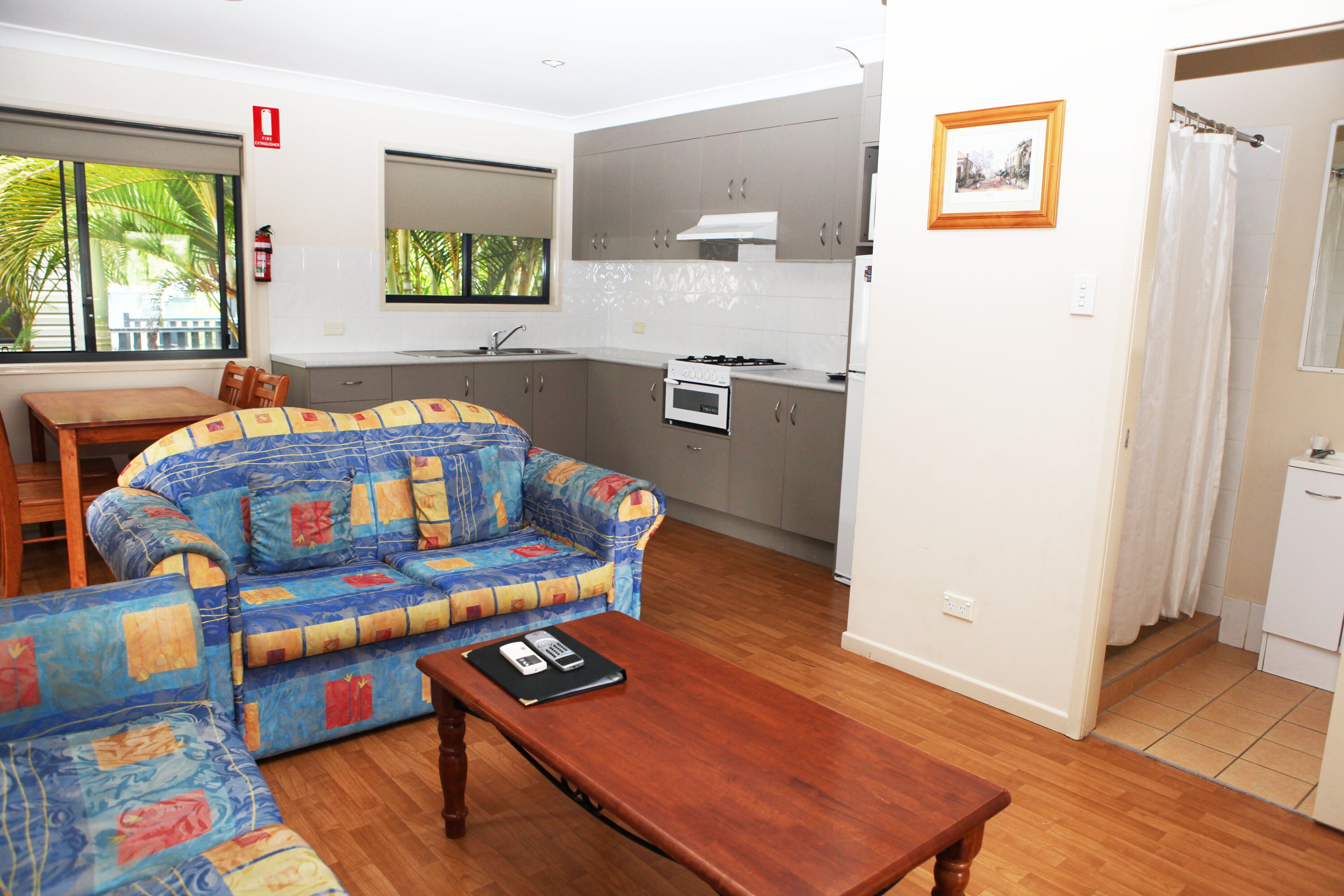 Una sala de estar con sofá, una mesa de centro de madera, y una zona de cocina con armarios y estufa.