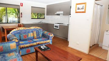 Una sala de estar con sofá, una mesa de centro de madera, y una zona de cocina con armarios y estufa.