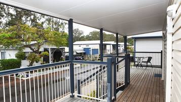 A covered outdoor deck with a railing, a table and chairs, and a view of the street and buildings in the background.