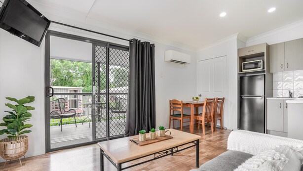 Un salon moderne comprenant un canapé, une table basse et un coin repas avec des chaises et une table. Il y a également un coin cuisine avec un réfrigérateur et un four à micro-ondes. Une porte-fenêtre coulissante donne accès à une terrasse extérieure avec une table et des chaises.