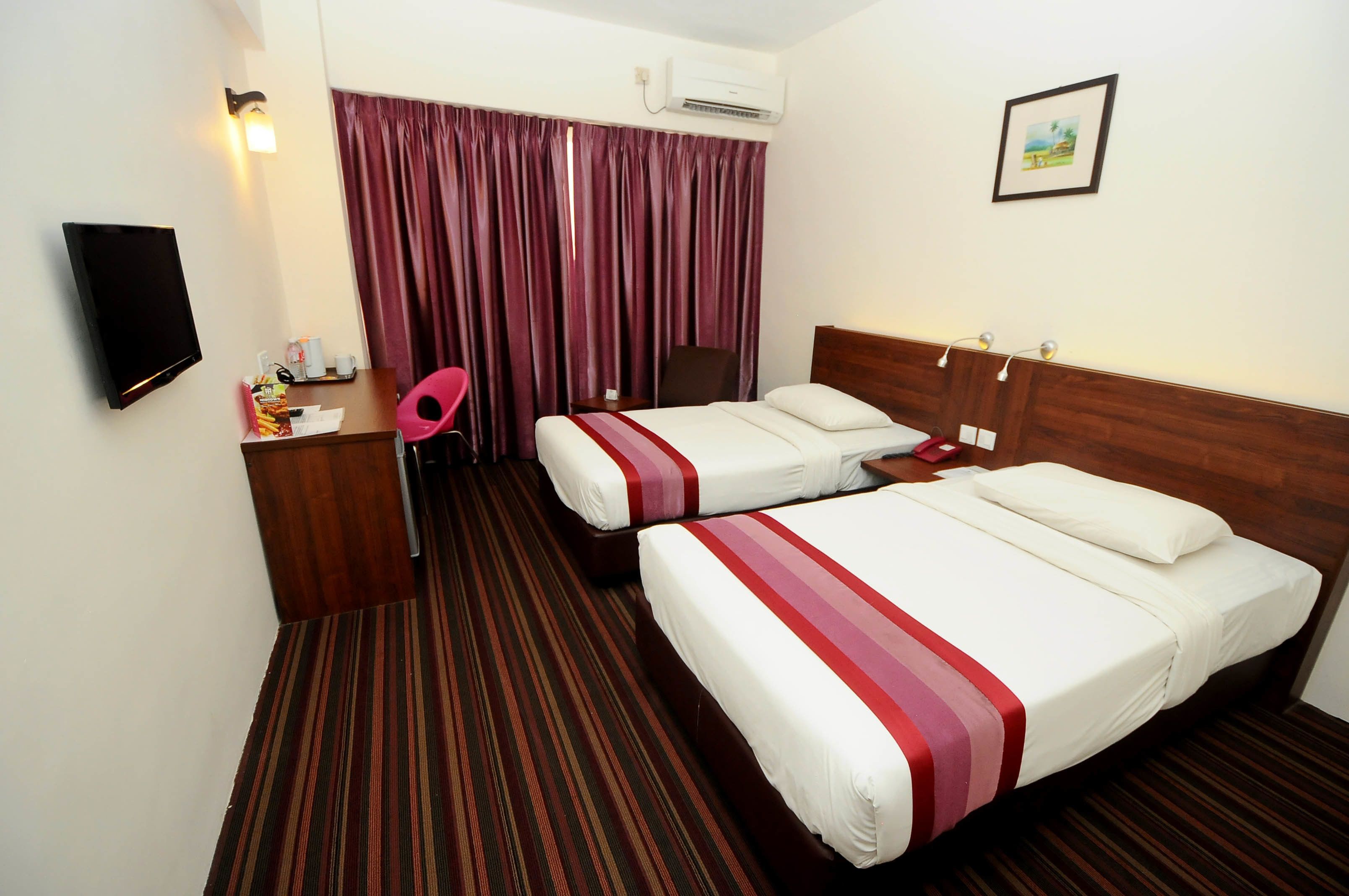 Habitación de hotel con dos camas, televisión, escritorio, silla y ventana con cortinas.