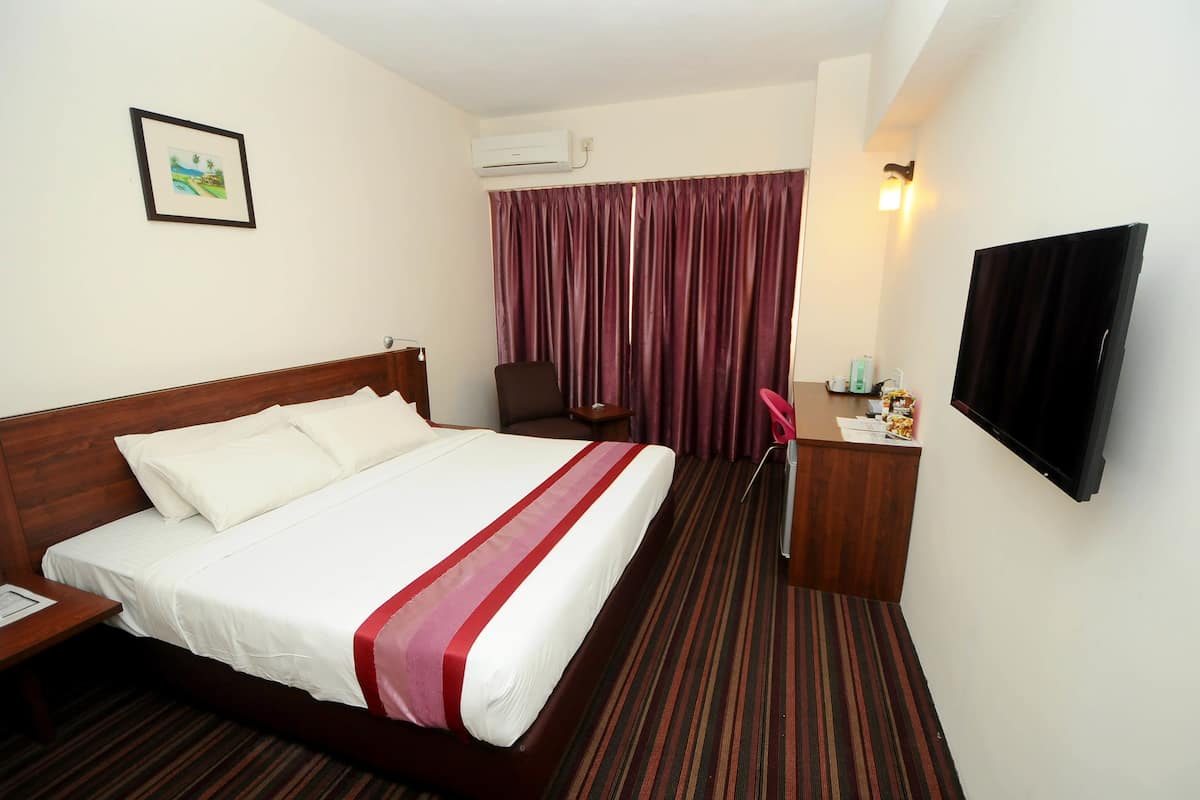 A hotel room with a large bed, a desk with a chair, a TV, and a window with curtains.