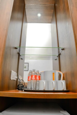 A compact hotel room with a wooden wardrobe, a small shelf with water bottles and mugs, and a glass shelf above. - Hotel YT Midtown (Kuala Terengganu)