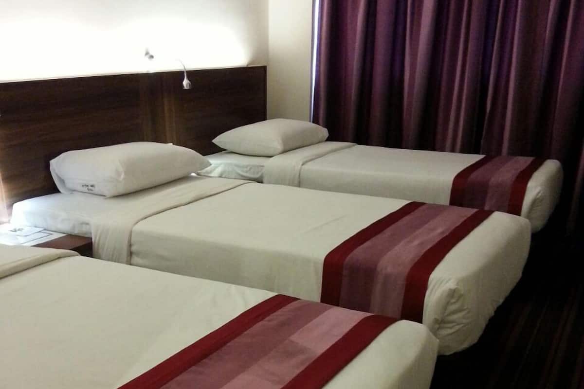 A hotel room with three beds, each with white bedding and red accents.