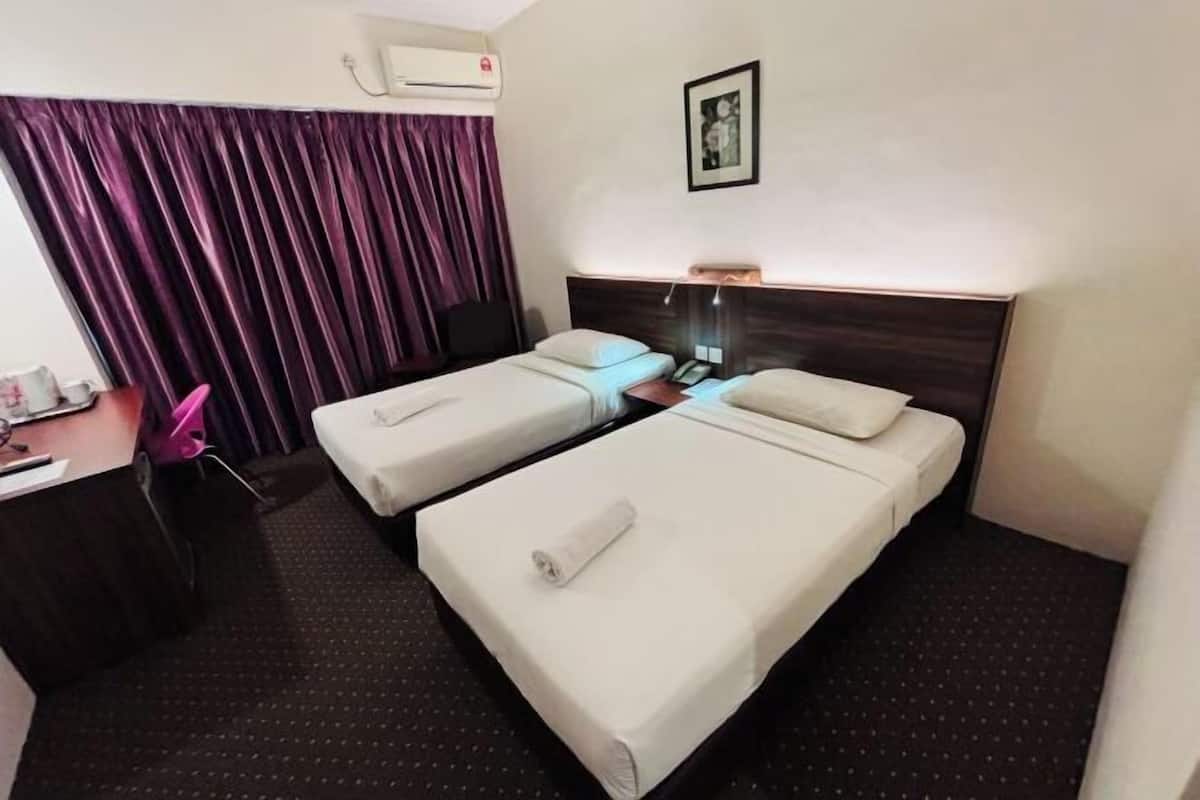 A hotel room with two single beds, a desk, a chair, and an air conditioning unit.