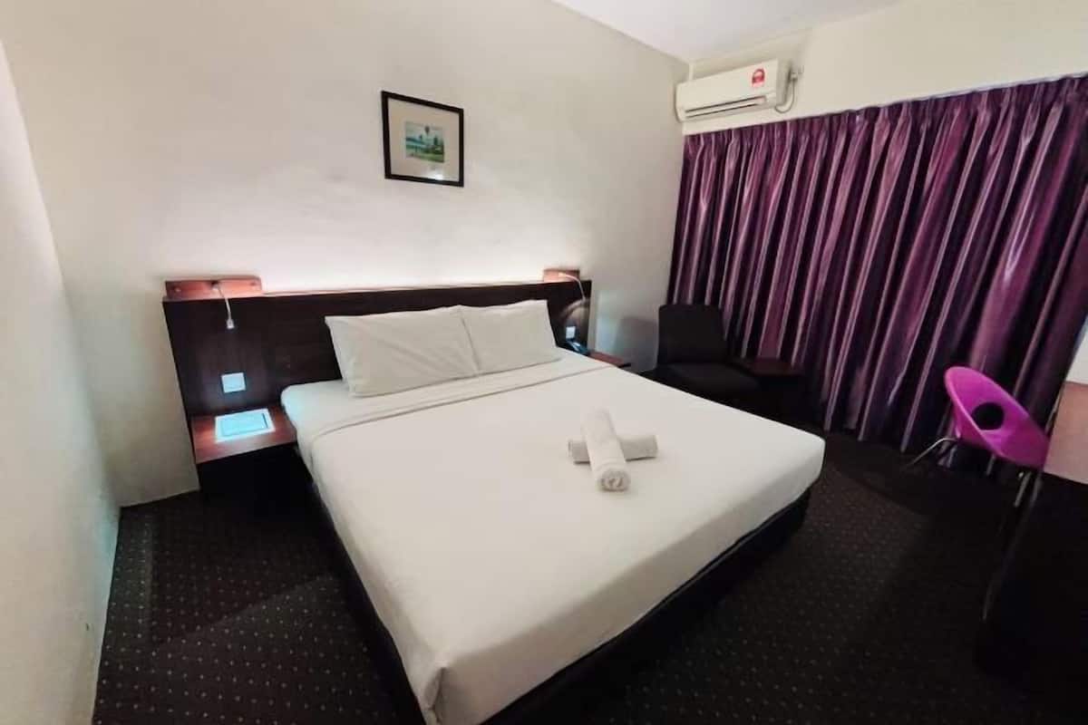 A hotel room with a bed, a nightstand, a chair, an air conditioning unit, and a curtain.