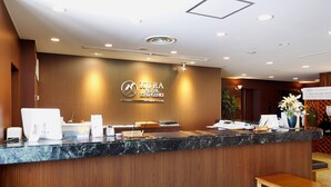 Una recepción de hotel con un mostrador de mármol, una caja registradora y una pantalla digital.