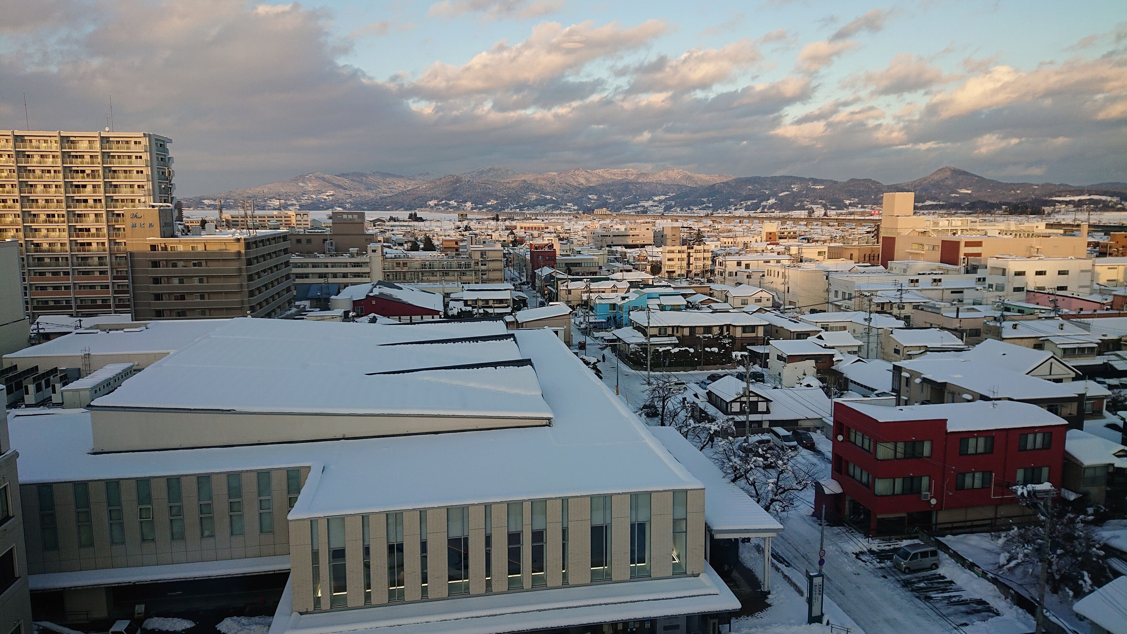A cityscape with snow-covered buildings, a mix of residential and commercial structures, and a mountainous backdrop.