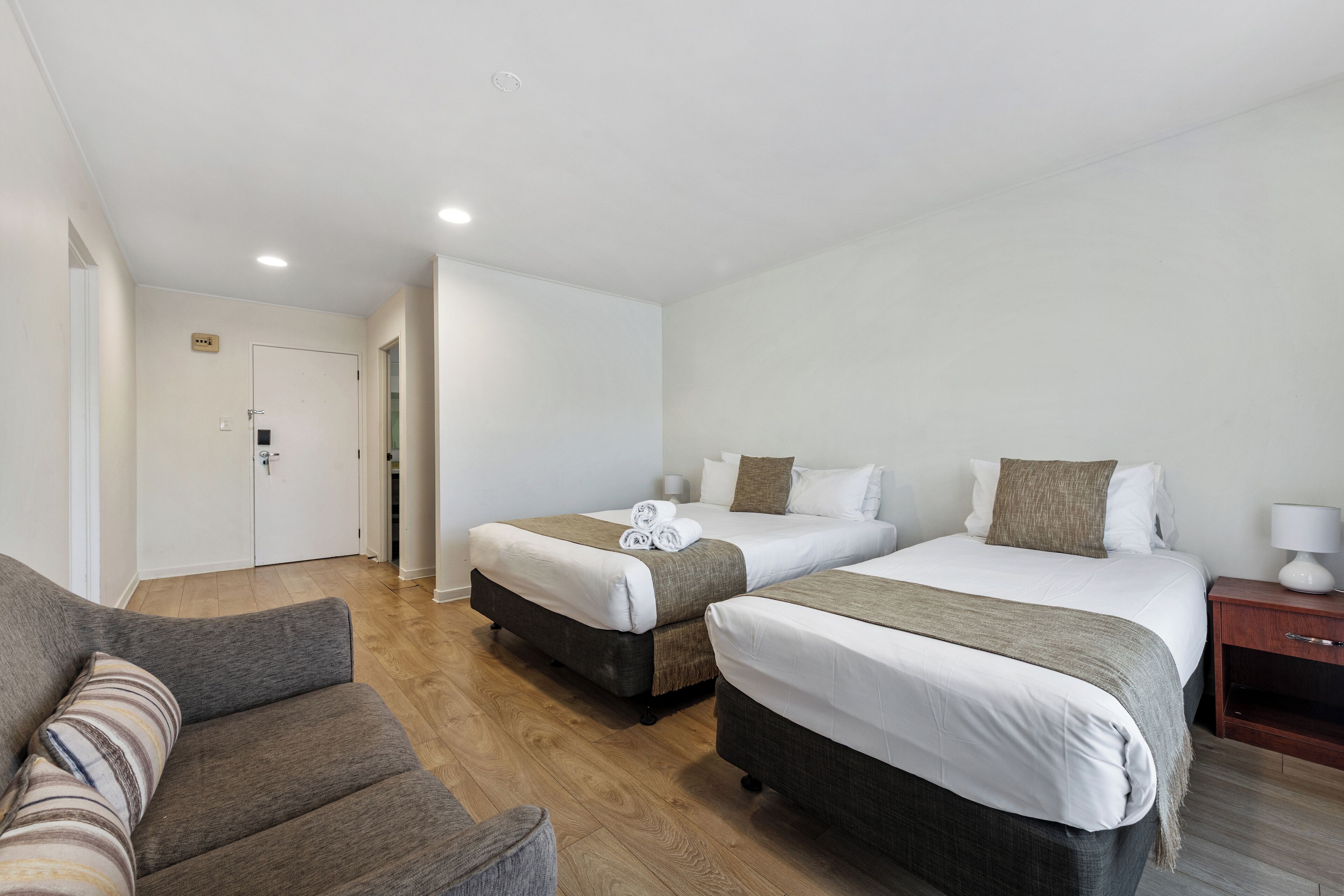 Une chambre d’hôtel avec deux lits, un canapé, un plancher en bois et une porte.
