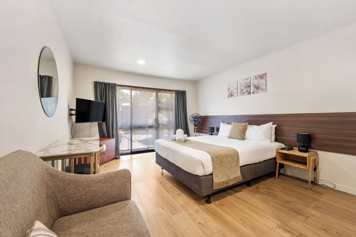Habitación de hotel con una cama, un escritorio, una silla, un televisor y un ventanal corredero al exterior.