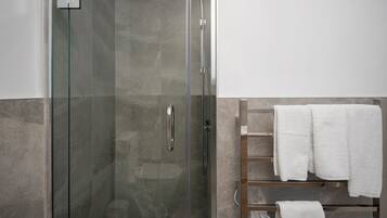 A modern bathroom with a glass-enclosed shower, a white towel rack, and a wooden shelf.