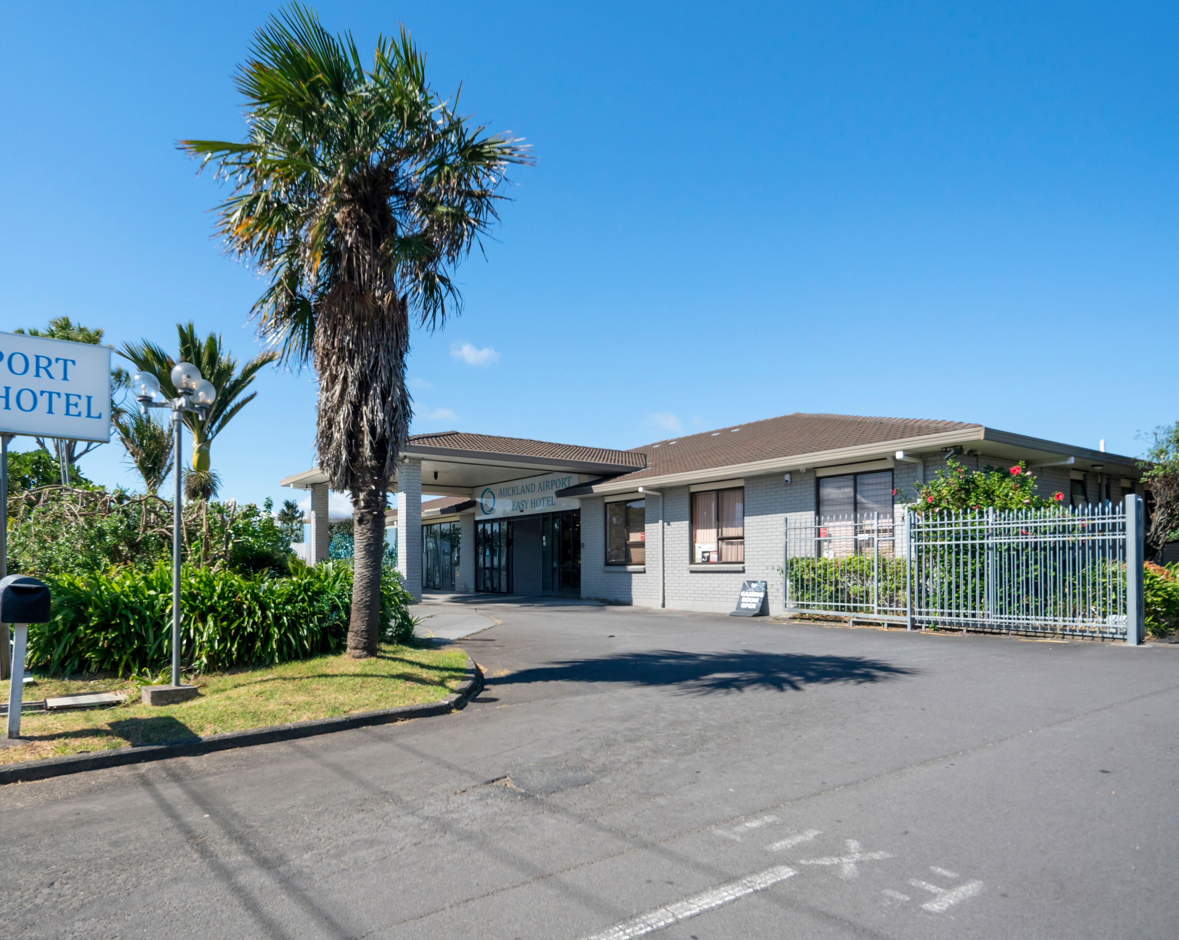 A hotel with a sign reading "Auckland Airport Easy Hotel," a covered entrance, and a parking area.