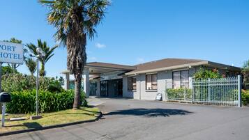 A hotel with a sign reading "Auckland Airport Easy Hotel," a covered entrance, and a parking area.