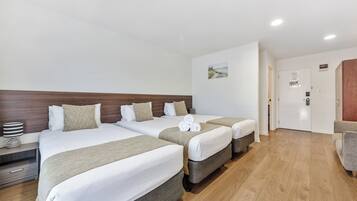 Ein Hotelzimmer mit drei Betten, einem Holzkopfstück, einem Gemälde an der Wand und Holzboden.