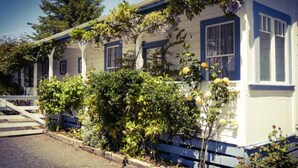 A two-story house with a porch, surrounded by lush greenery and flowering plants. - Tongariro Crossing Lodge (National Park Village)