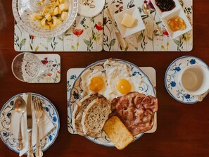 Een ontbijtsetting met een bord eieren, spek, toast en fruit op een tafelkleed met bloemen.