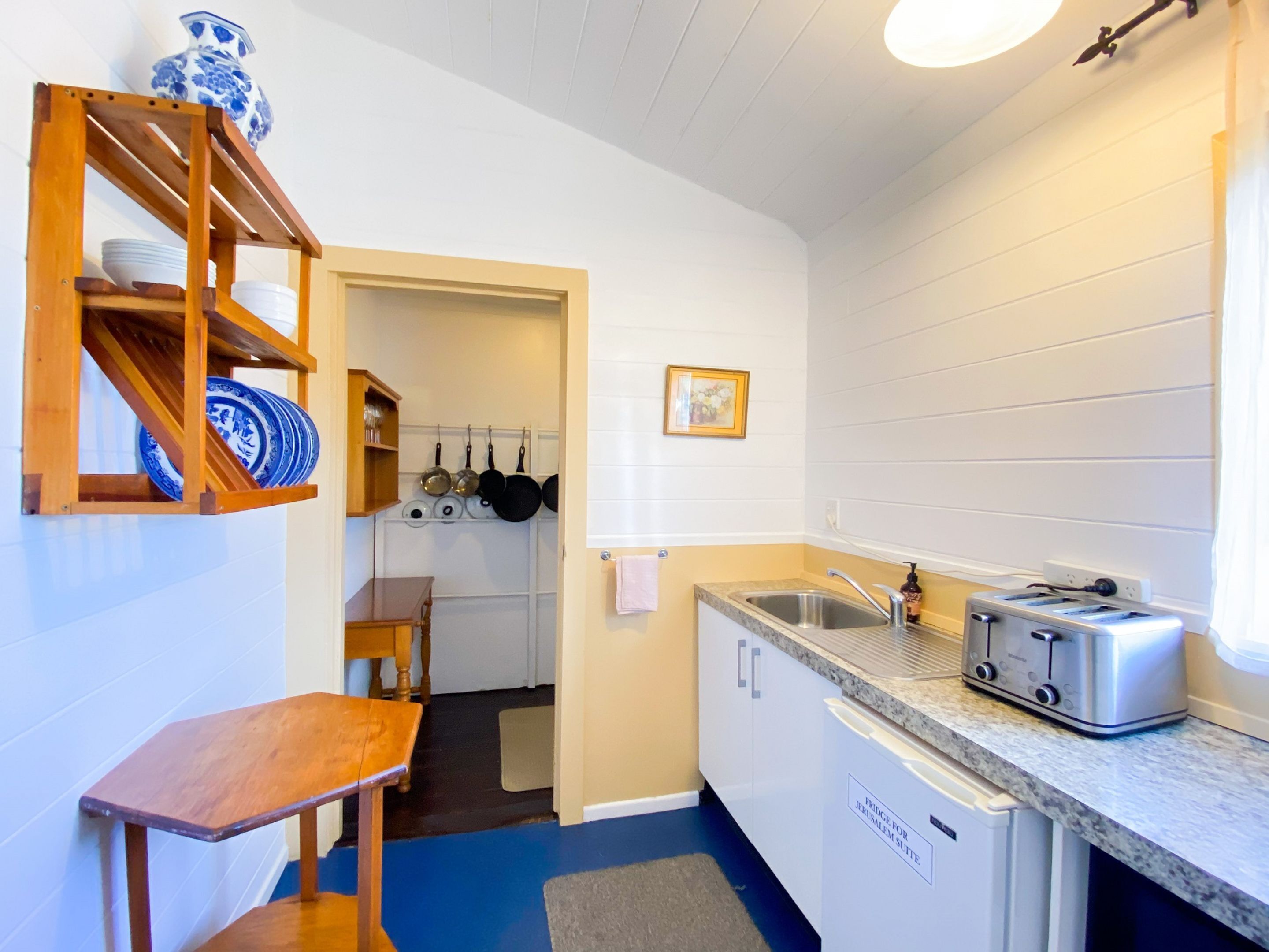 A compact kitchen with a wooden shelf holding plates, a sink with a faucet, and a toaster.